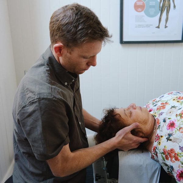 Chiropractor performing a gentle neck adjustment on a patient lying on a treatment table in a calm, light-filled clinic room.